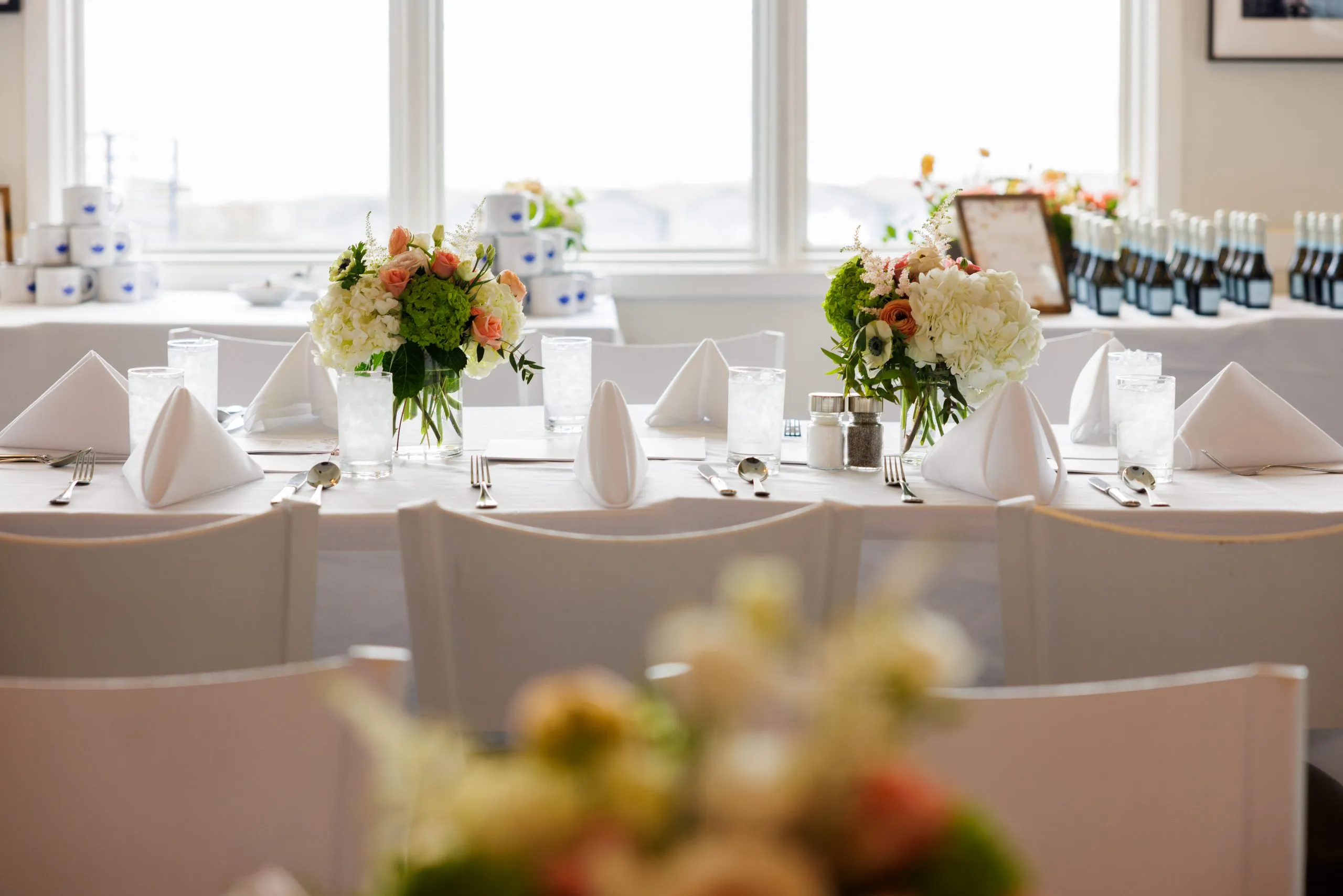 Elegant private dining setup at Drift House, featuring beautifully arranged floral centerpieces, crisp white linens, and ocean-view windows—perfect for special events and celebrations.